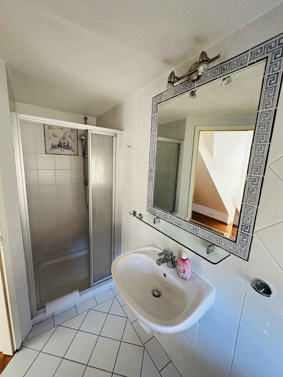 Badezimmer mit Dusche, Waschbecken und Spiegel mit Muster