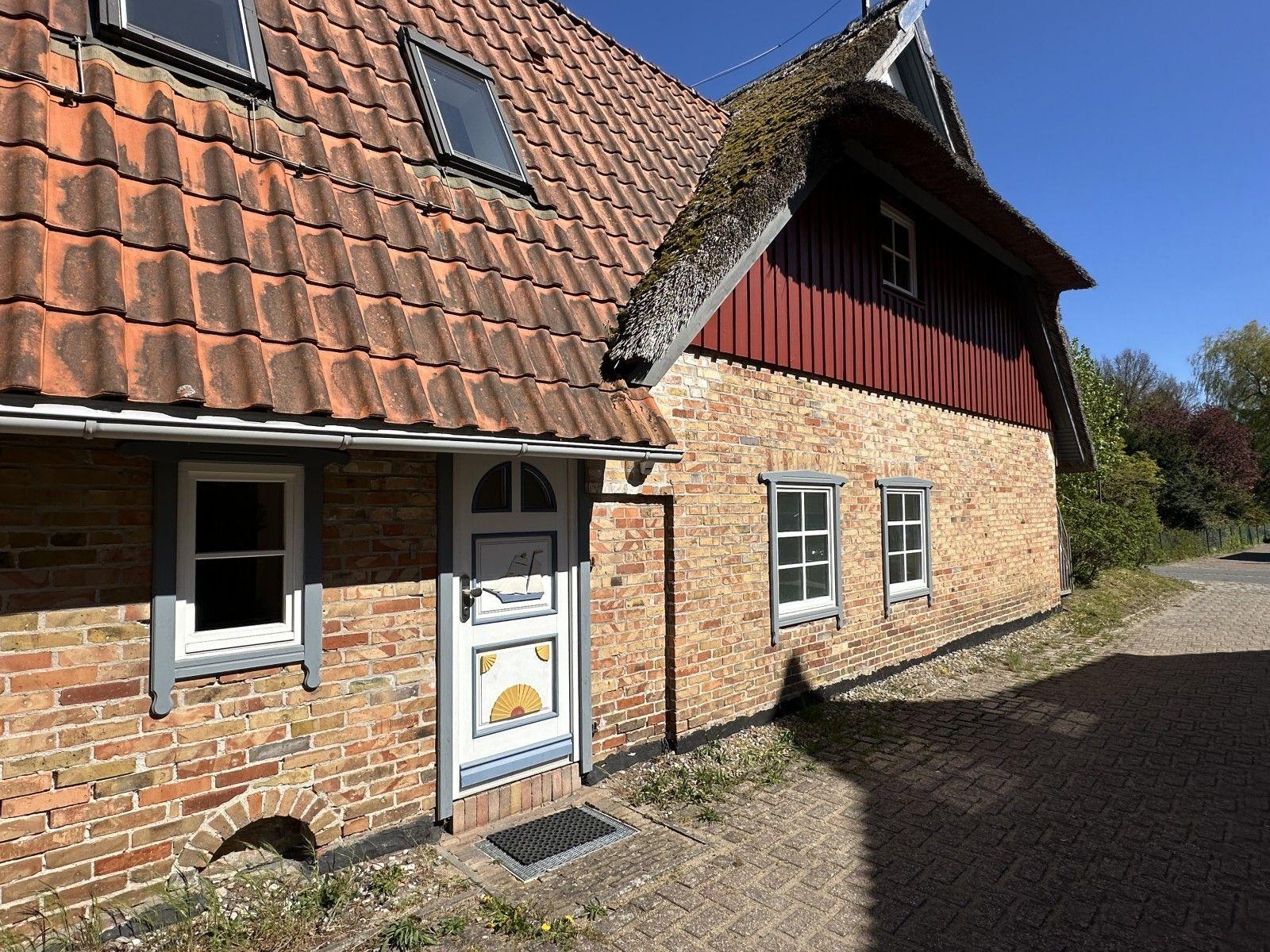 Haus mit Ziegeldach, rotem Schindelteil und Steinmauer. Weiße Tür mit Dekoration.