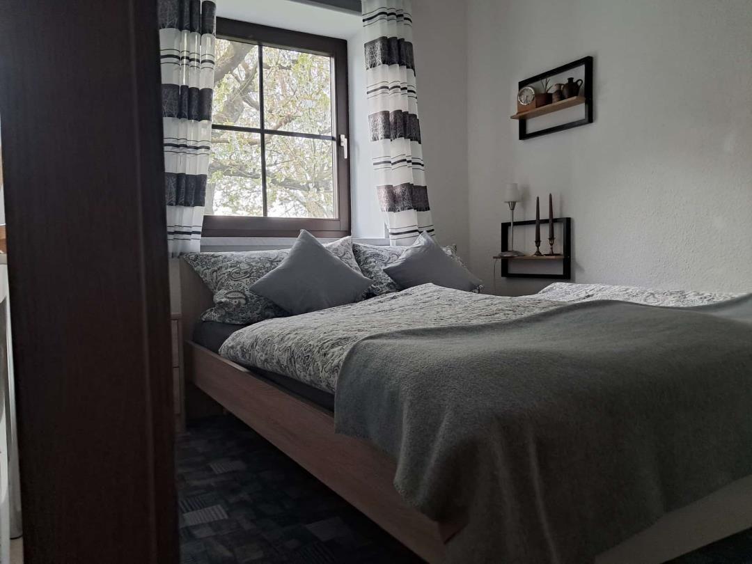 Schlafzimmer mit Bett, Fenster und Gardinen.