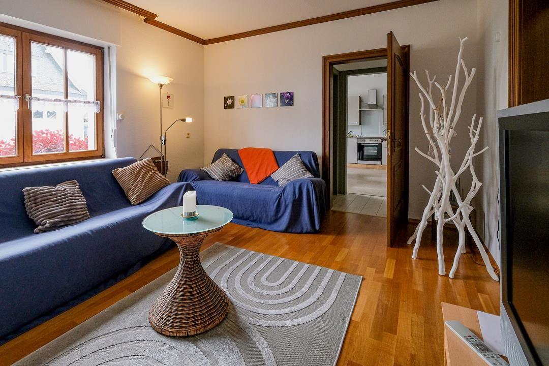 Wohnzimmer mit blauem Sofa, Holzboden und Blick in die Küche.