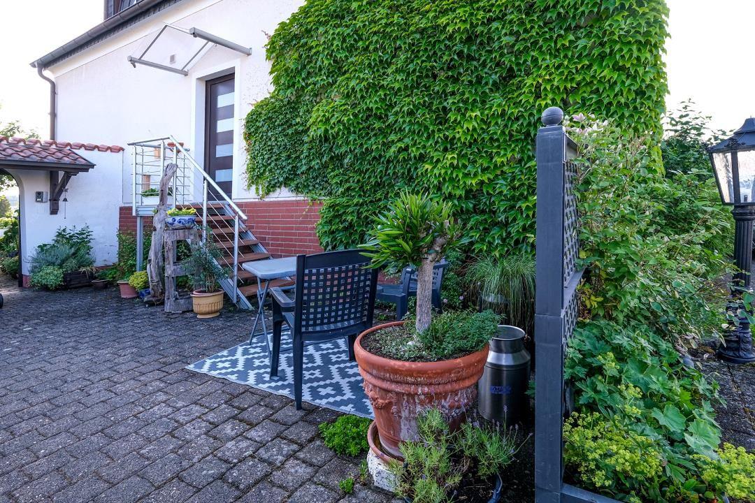 Hinterhof mit Tisch, Stühlen und Pflanzen. Steinplattenboden und Efeubewuchs an der Wand.