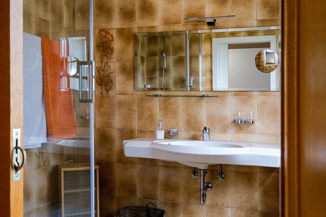 Bad mit Dusche, Waschbecken und Spiegel an Wand mit Fliesen