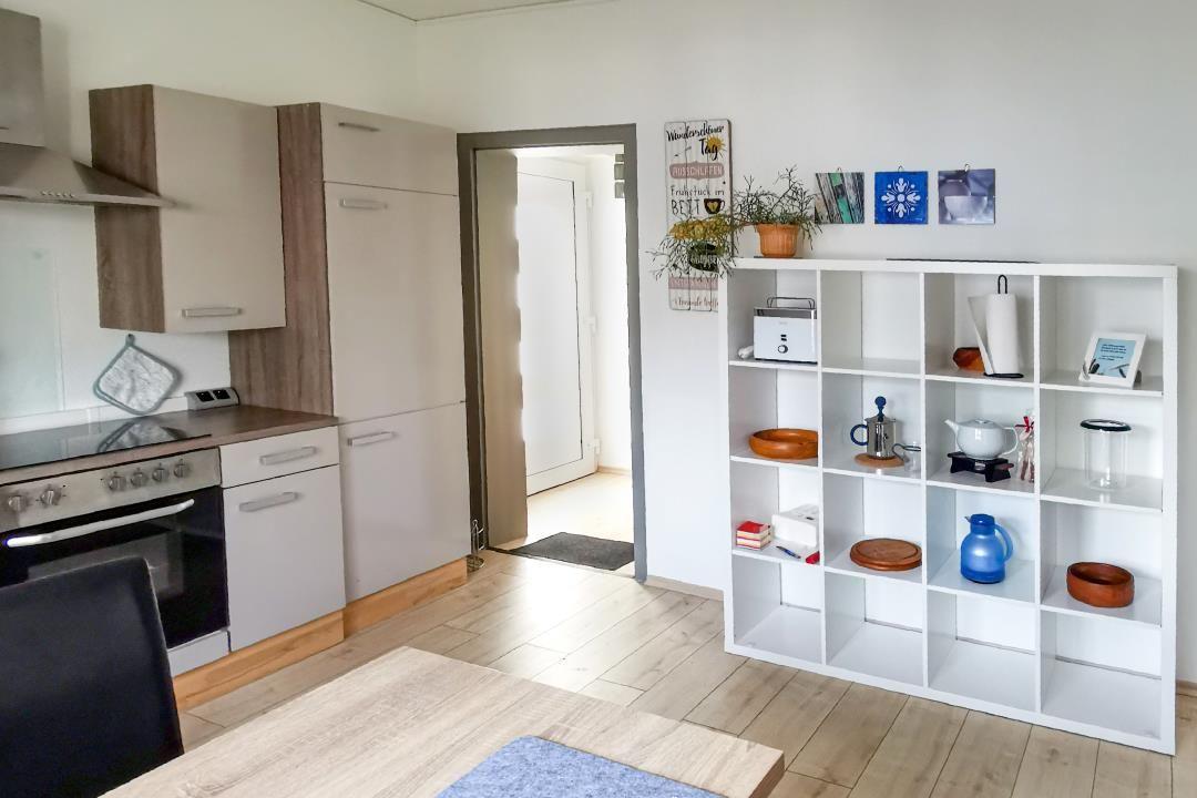 Küche mit Holzboden und weißen Schränken. Regal mit Geschirr und Dekoration.