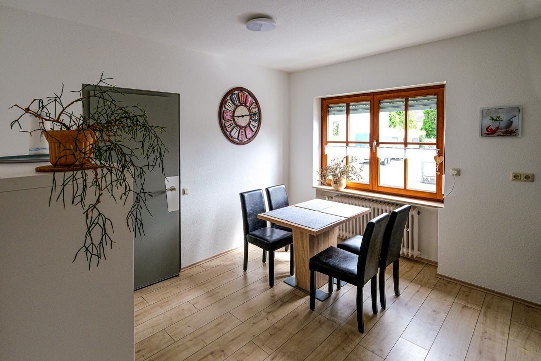Esszimmer mit Tisch, Stühlen, Fenster und Wanduhr.