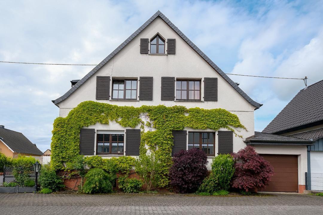 Ein zweistöckiges Haus mit dunklen Fensterläden und Kletterpflanzen an der Fassade.