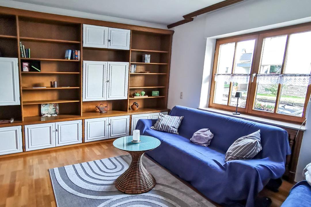 Ein Wohnzimmer mit blauem Sofa, Holzregalen und großem Fenster.