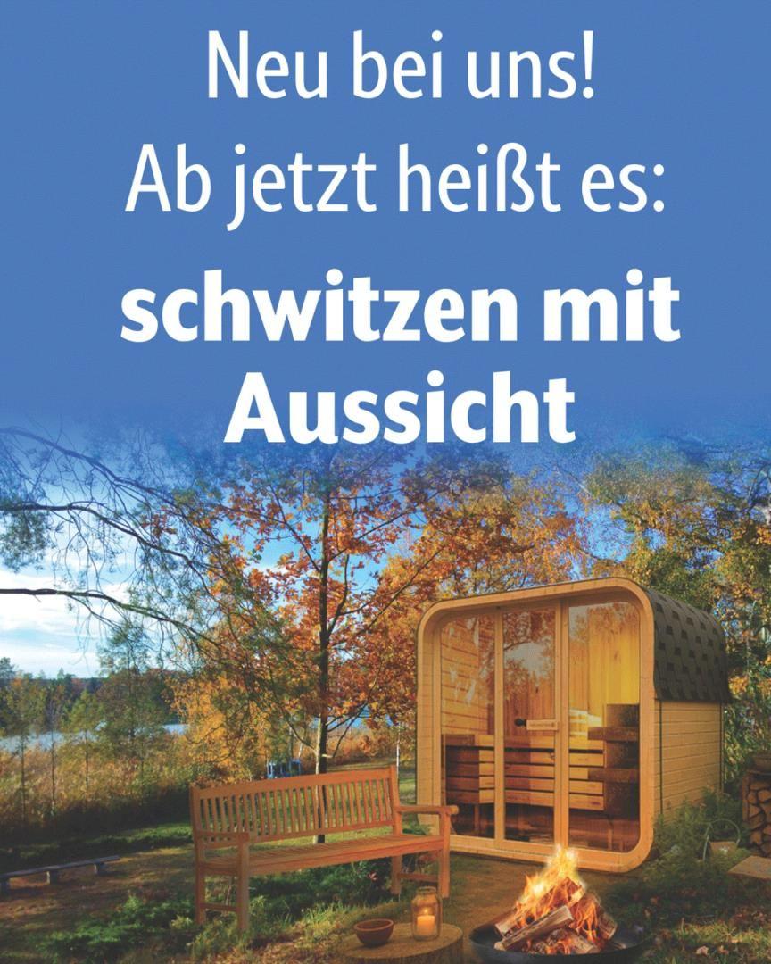 Außenliegende Sauna mit Blick auf Wald und See. Holzbank und kleiner Feuerkorb.