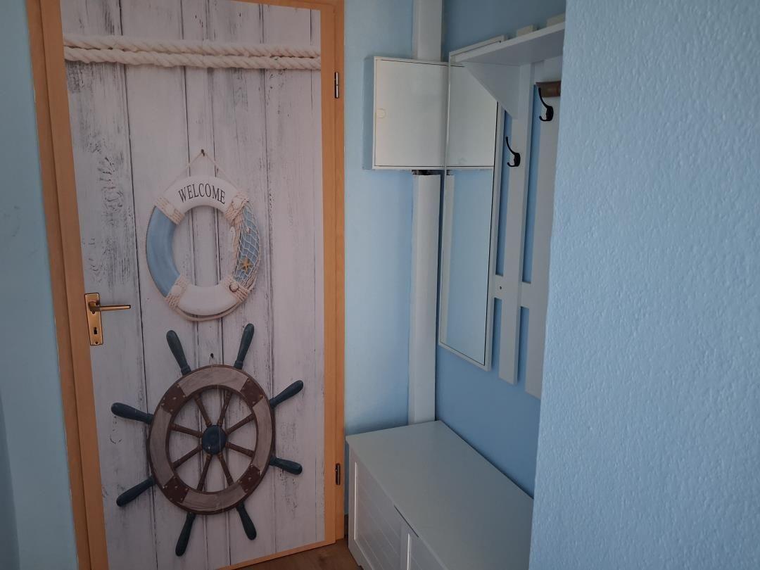 Tür mit Segelruder und Willkommensring. An der Wand hängt ein Spiegel und ein Haken.