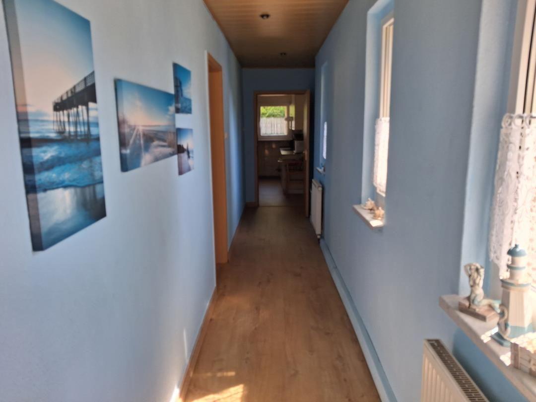 Flur mit Holzboden, blauen Wänden und Fenstern. Wandbilder zeigen Meereslandschaften.