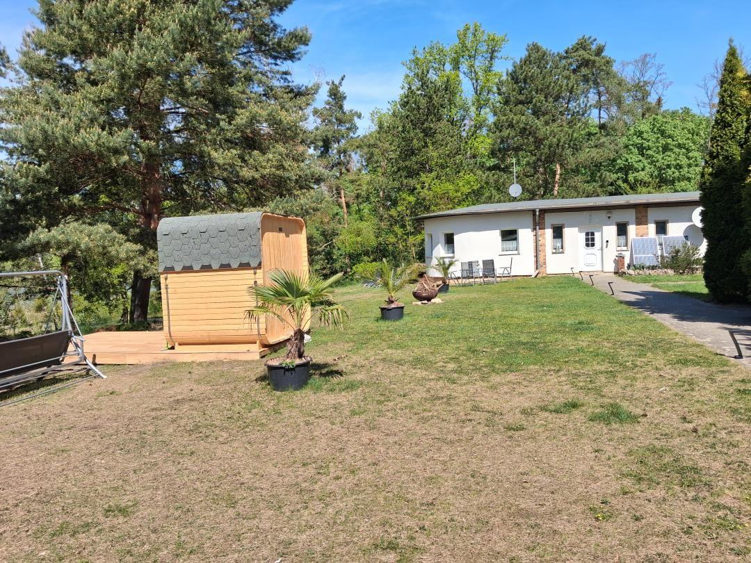 Haus mit Garten, Sauna und Bäumen im Hintergrund.