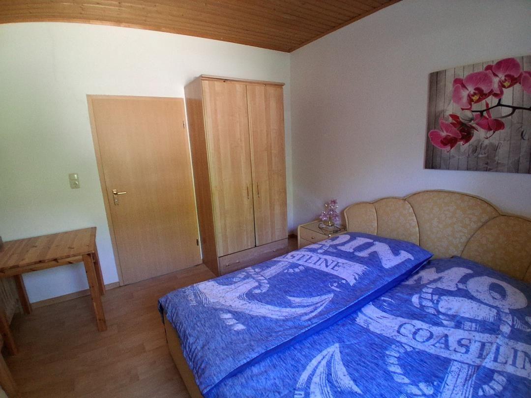 Schlafzimmer mit Bett, Kleiderschrank und Wandbild mit Orchidee.