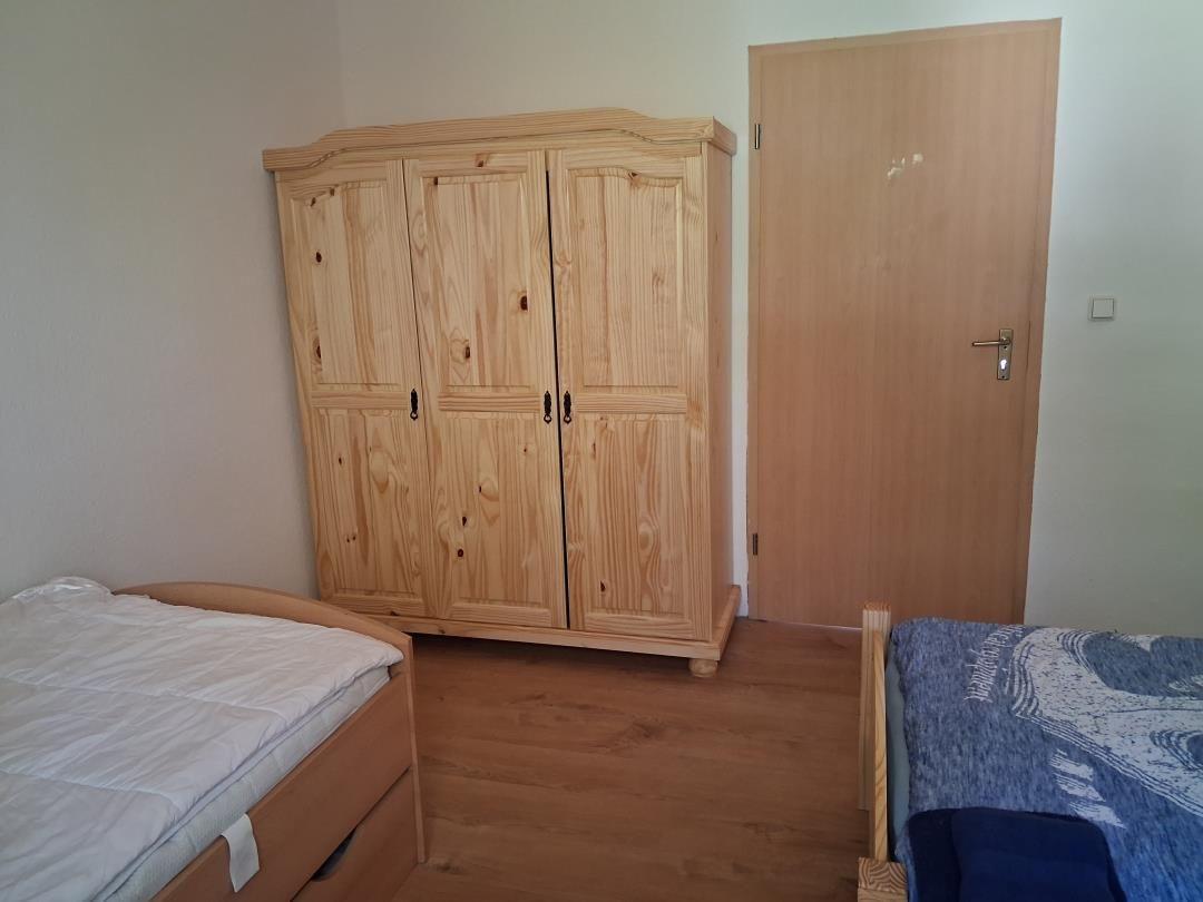 Zimmer mit zwei Betten und einem Holzschrank. Holzfußboden und Tür.