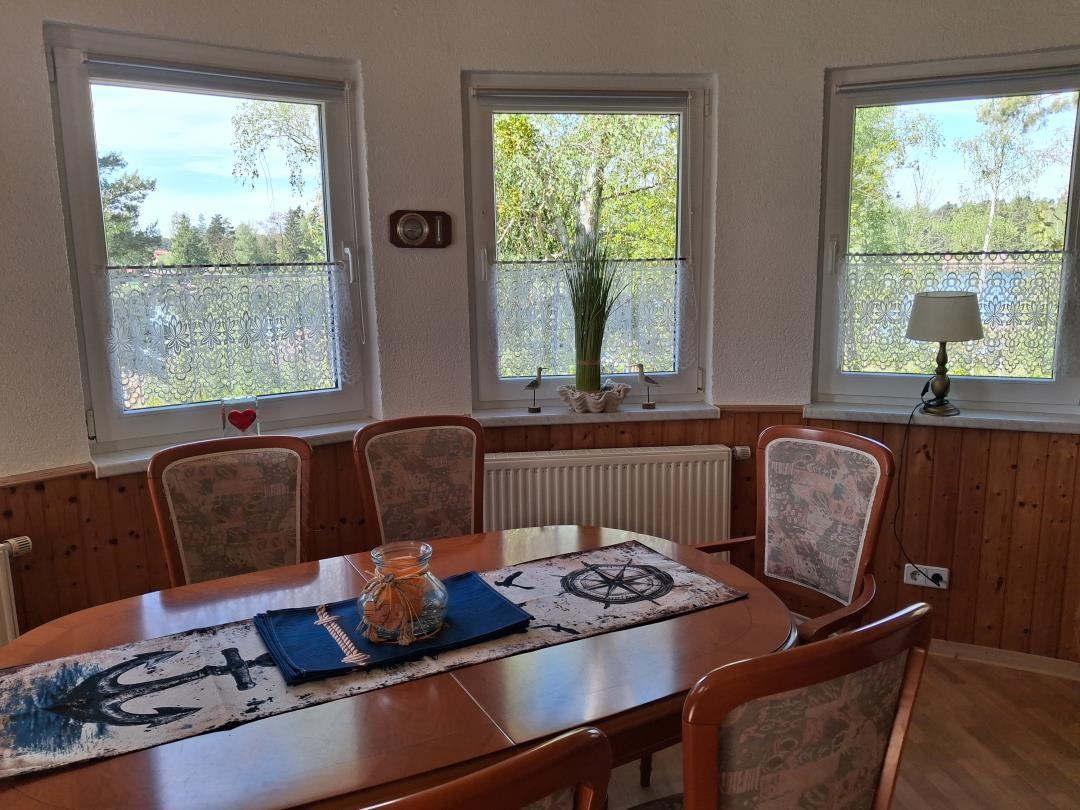 Esszimmer mit Holztisch, Stühlen und Fenstern mit Blick auf Wald.