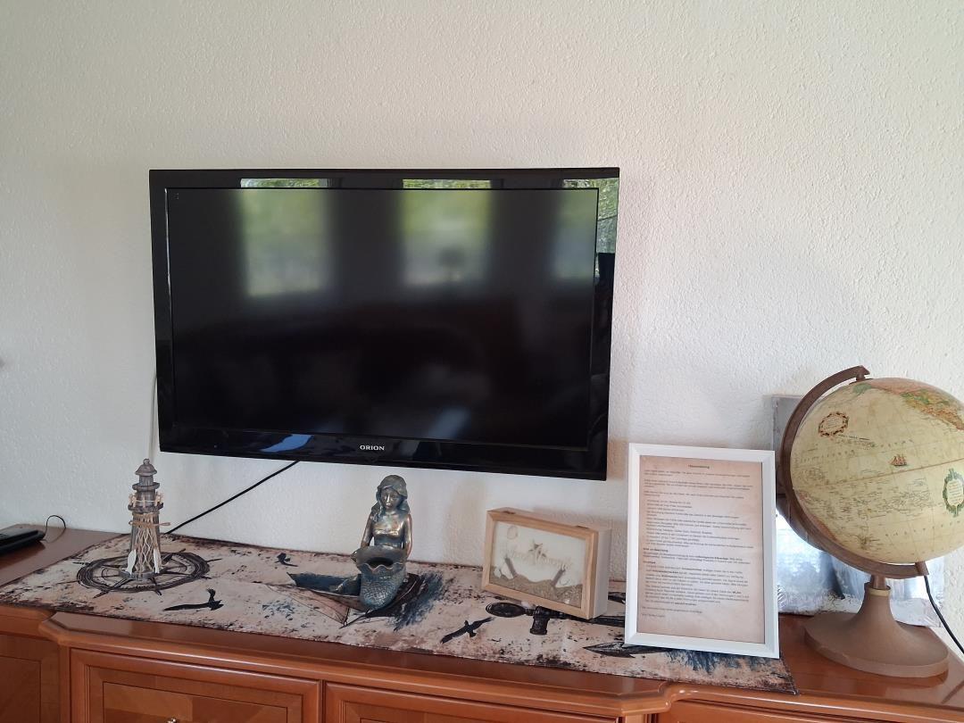 Flachbild-TV auf Holzboard mit Globus und Dekorationsobjekten.