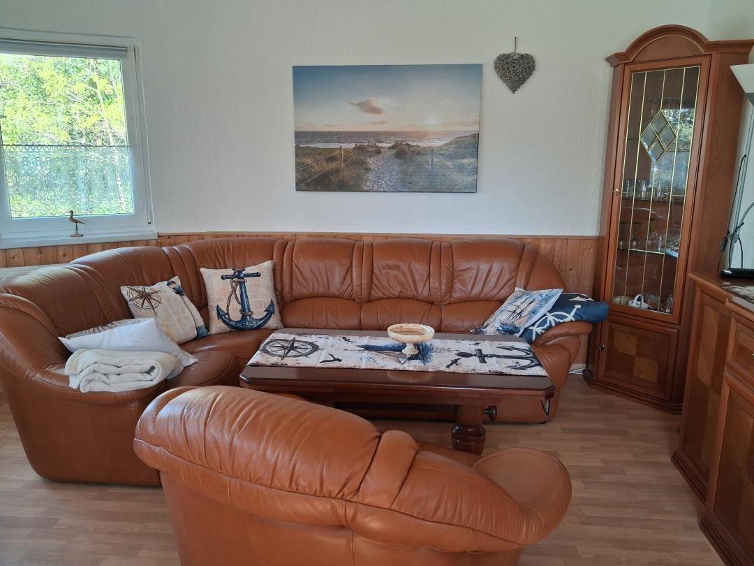 Ein Wohnzimmer mit braunem Ledersofa, Holztisch und Glasvitrine.