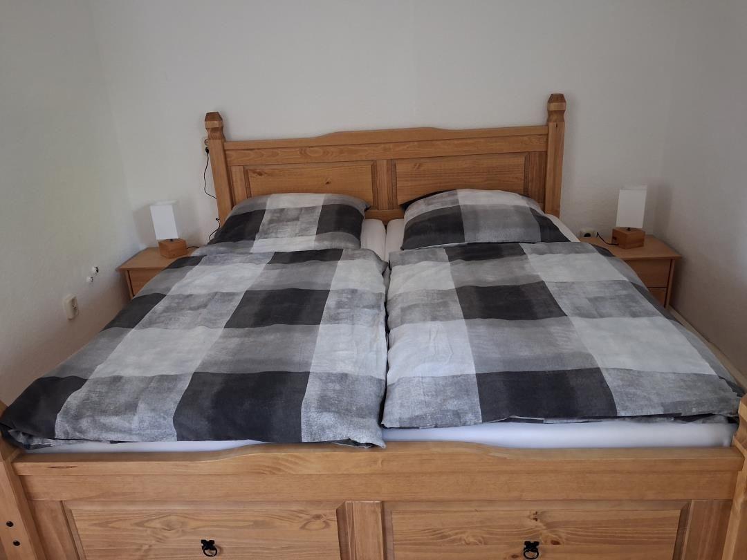 Double bed with wooden frame and checkered bedspread. Two nightstands with lamps.