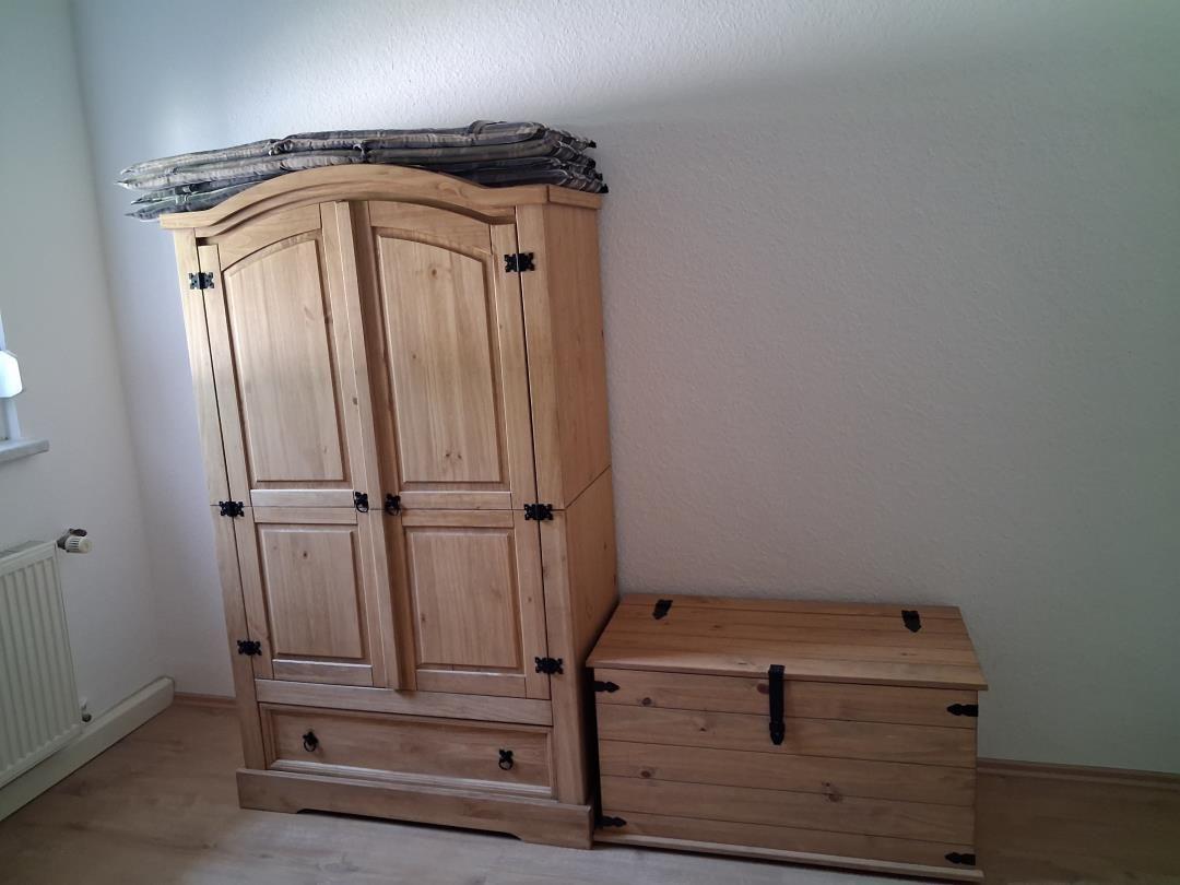 Wooden wardrobe with two doors and drawer, next to wooden chest with lid.