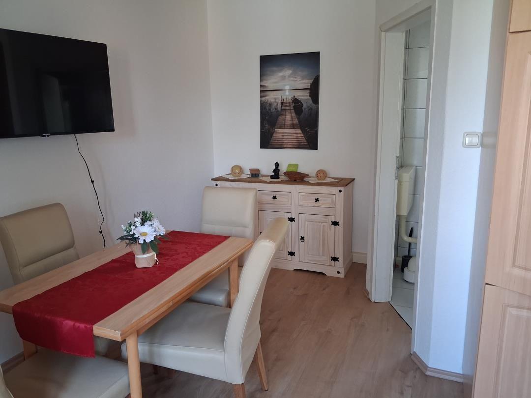 Dining area with table, chairs, and TV. Wall artwork. View into bathroom.