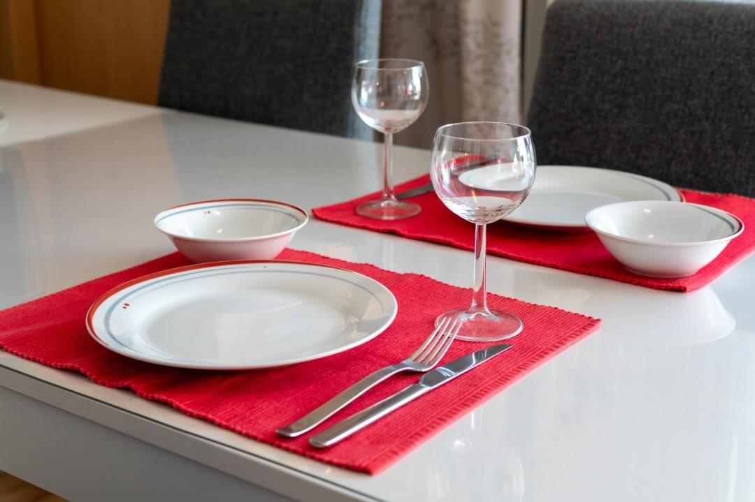 Tisch mit roten Untersetzer, weißen Tellern, Gläsern und Besteck.