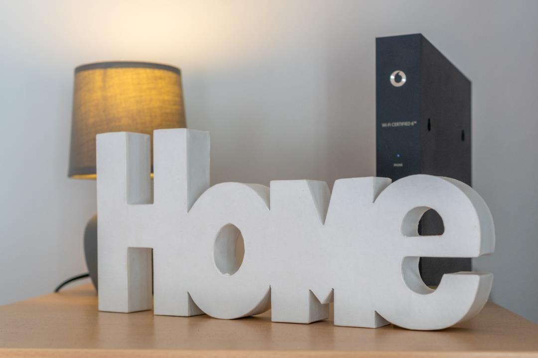 Wohnzimmer mit weißem Home-Schild, Lampe und WLAN-Router auf Tisch.