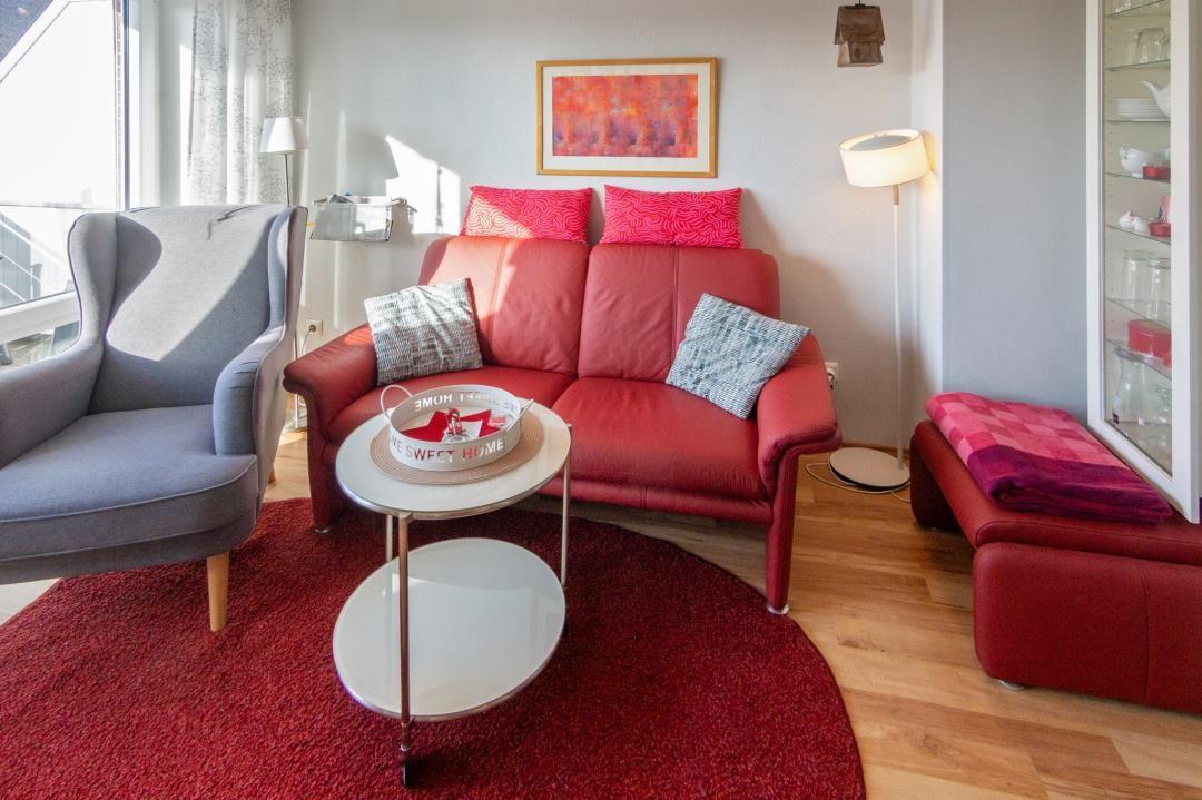 Ein Wohnzimmer mit rotem Sofa, grauer Sessel und runder Teppich.