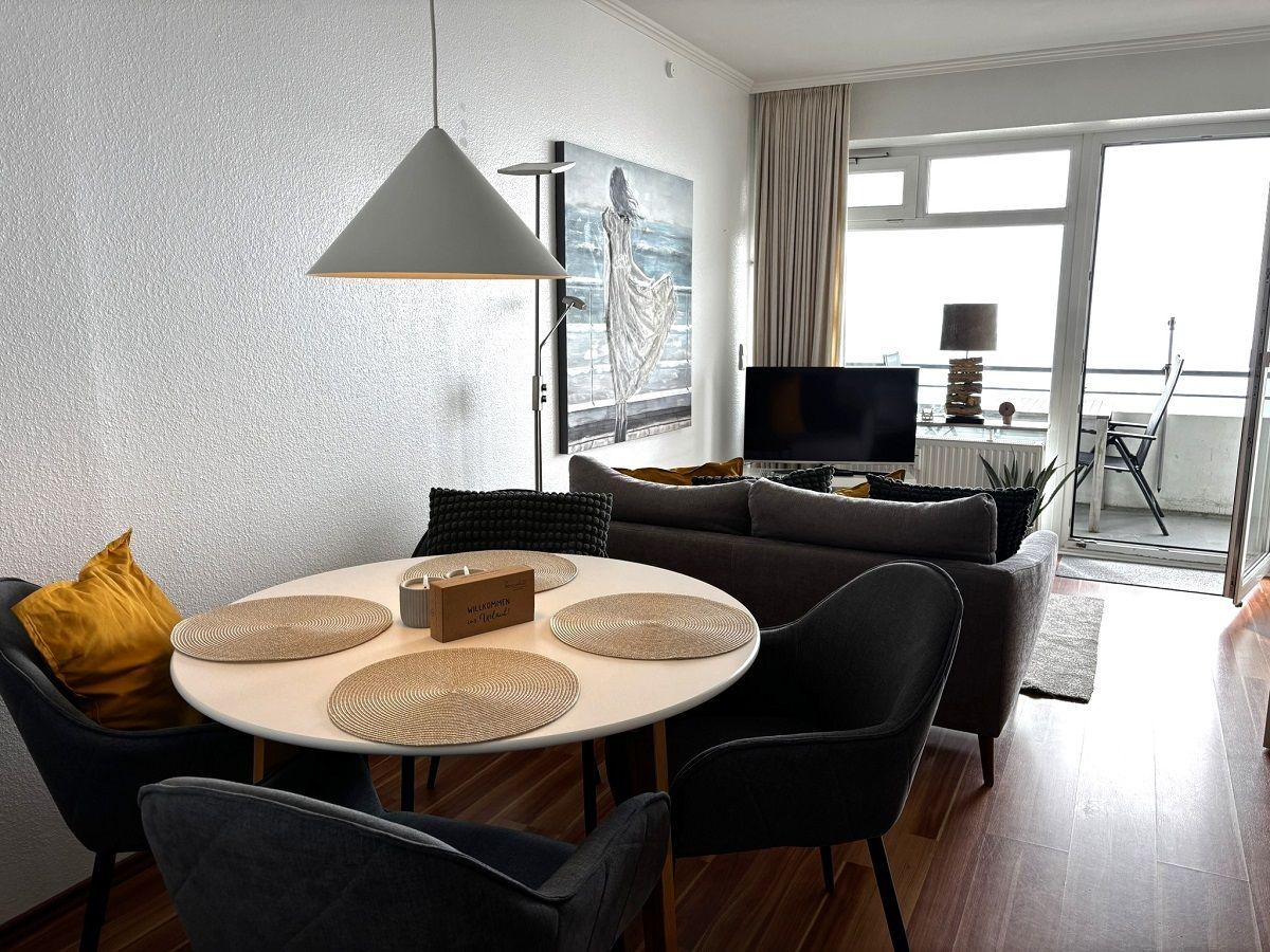 Rundes Esszimmer mit Tisch, Stühlen und Wandbild. Wohnbereich mit Sofa und TV. Balkon mit Sicht auf Stadt.