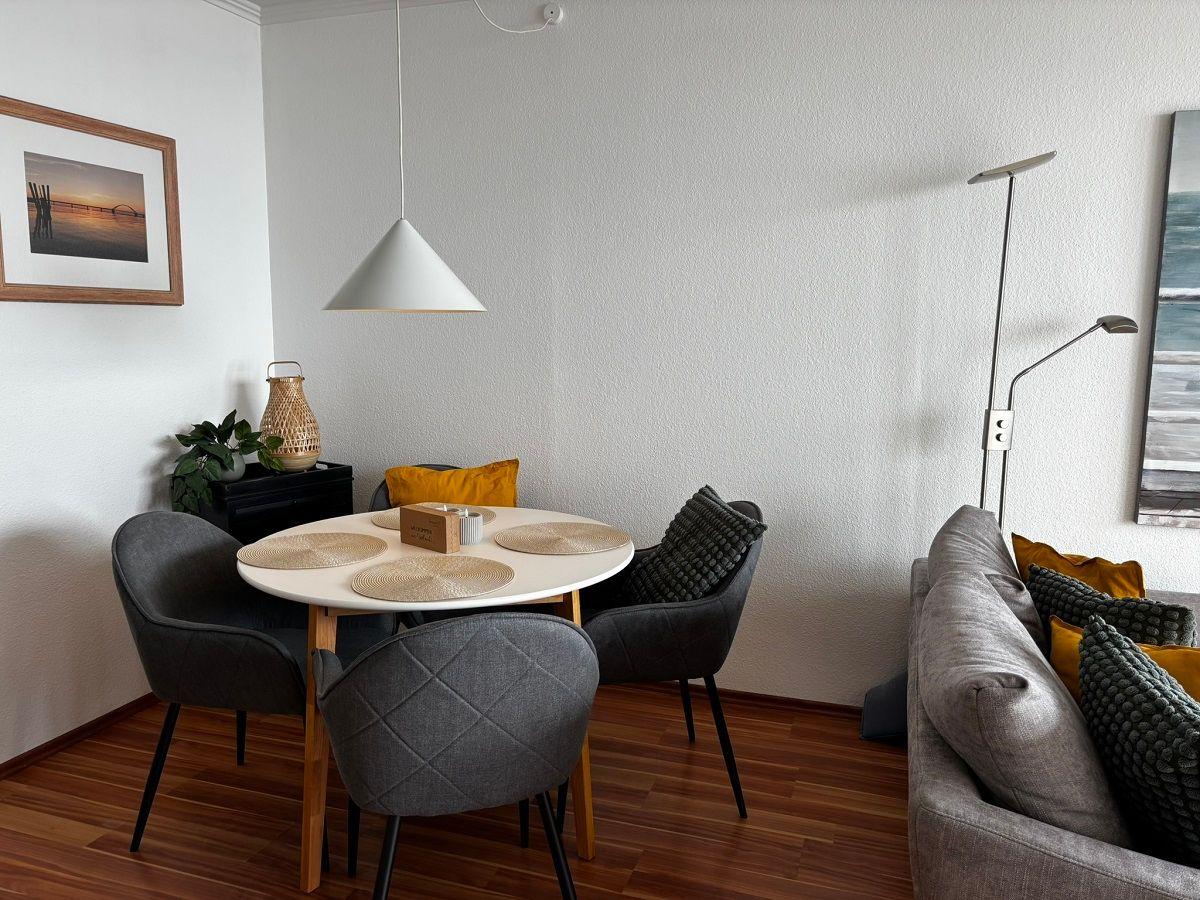 Rundtisch mit vier Stühlen, Sofa mit Kissen und Stehlampe im Wohnbereich.