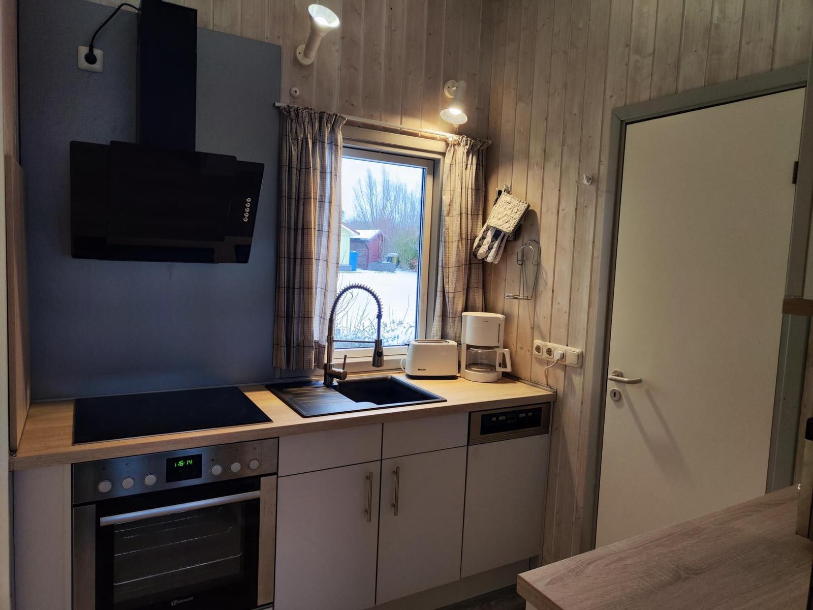 Kitchen with stove, sink, and window. Wooden walls and kitchen counter.