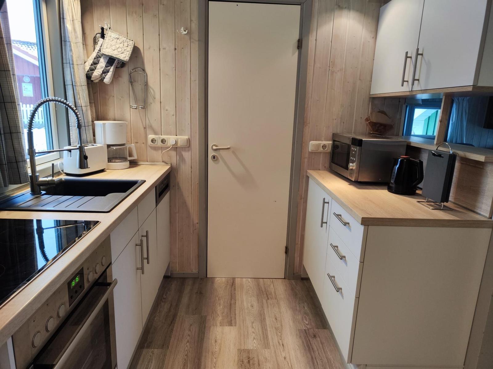 Kitchen with countertops, sink, stove, and microwave. Wooden walls and floor.