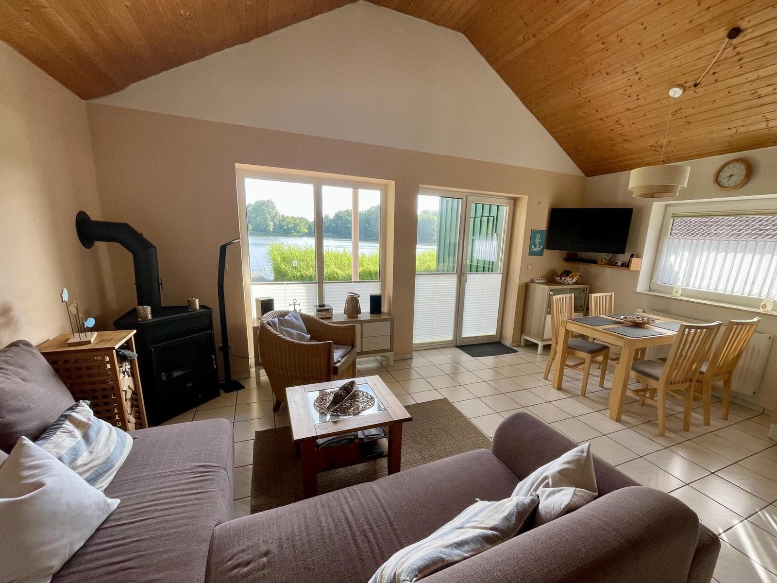 Living and dining area with wooden ceiling, fireplace, and view of water.