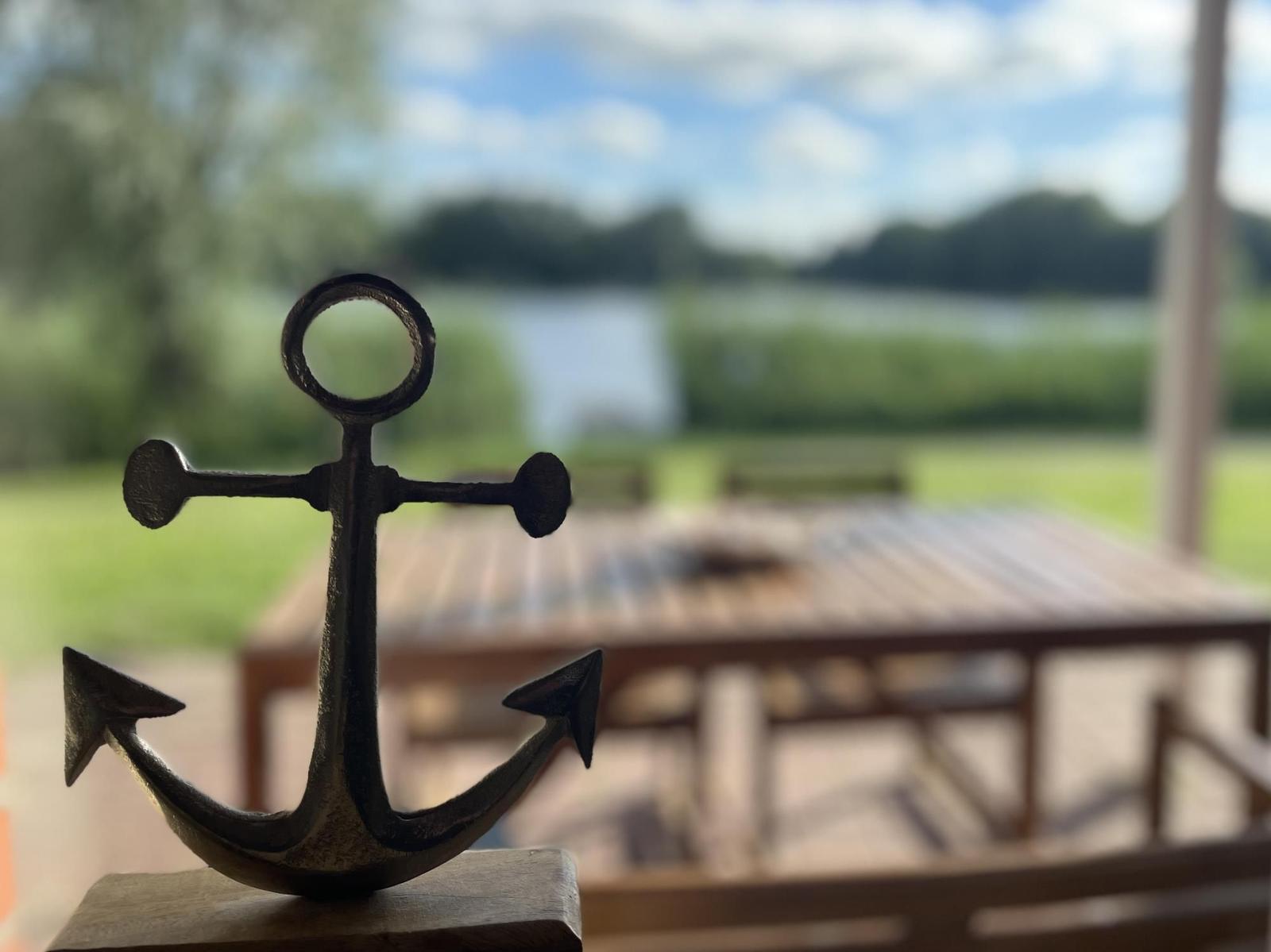 A small anchor sits on a wooden block. In the background, a patio with a table overlooks water and greenery.