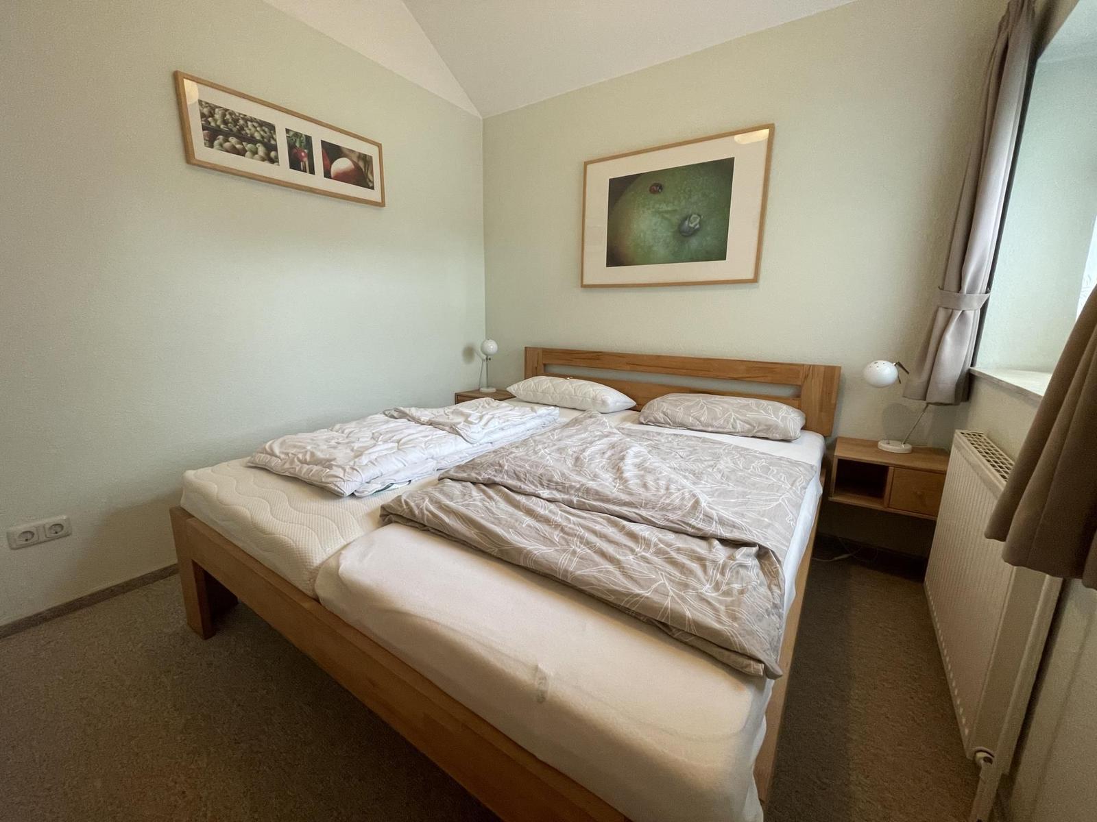 A bedroom with a double bed, two bedside tables, and wall pictures.