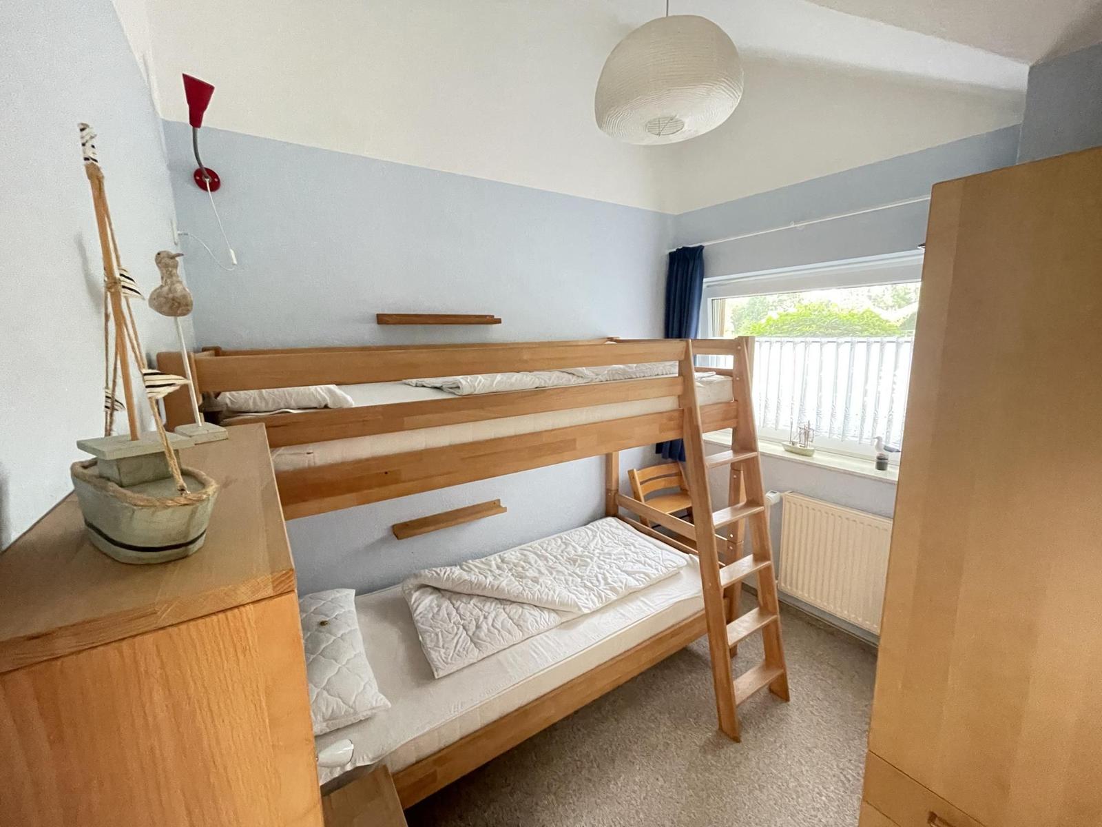 A bedroom with a wooden bunk bed, a window, and a wardrobe.