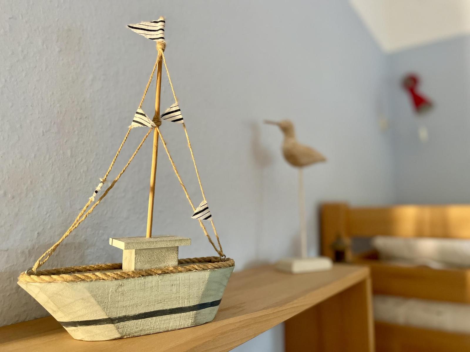 A wooden sailboat with striped flags sits on a table next to a bird figurine.