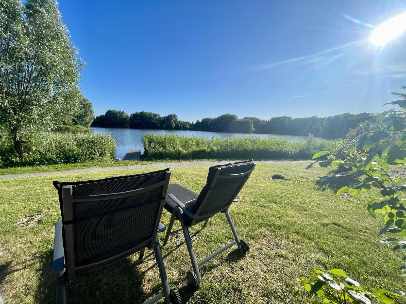 Two lounge chairs on a lawn with a view of a lake and trees.