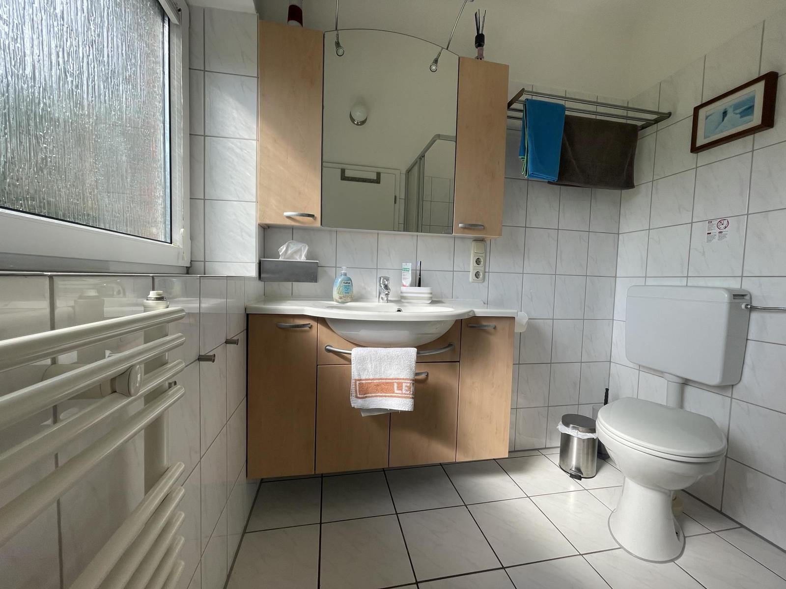 Bathroom with sink, toilet, and window. Wooden cabinets and tiles.