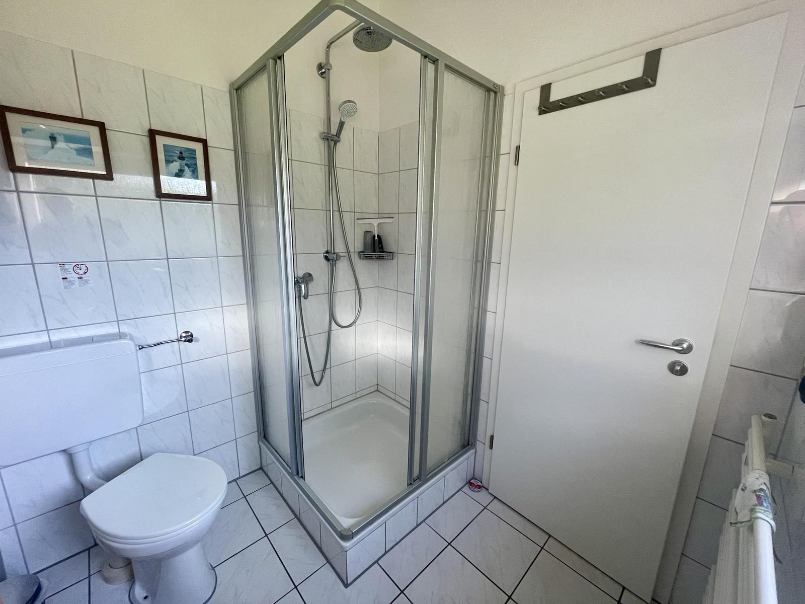 Bathroom with shower, toilet, and white tiles.