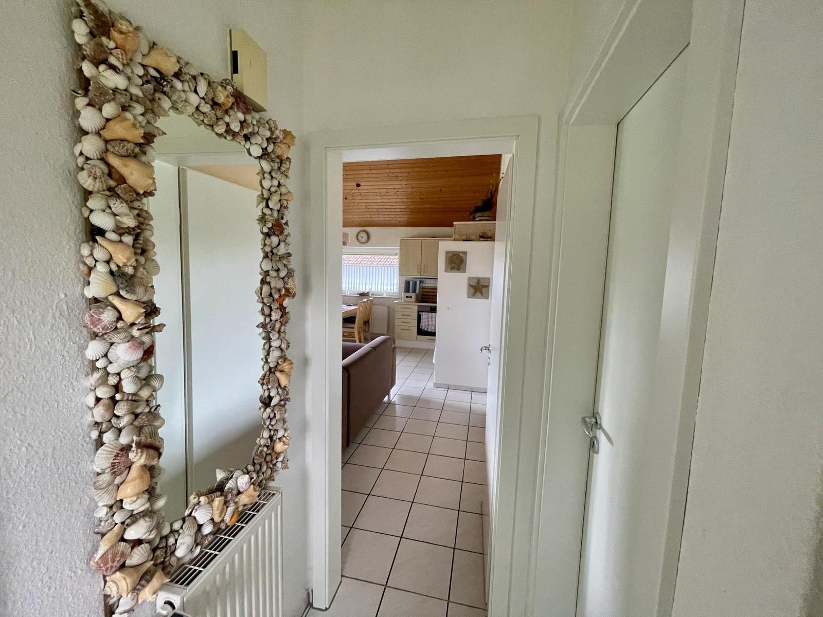 Mirror with shell frame in hallway. View into kitchen and living area with wooden ceiling.