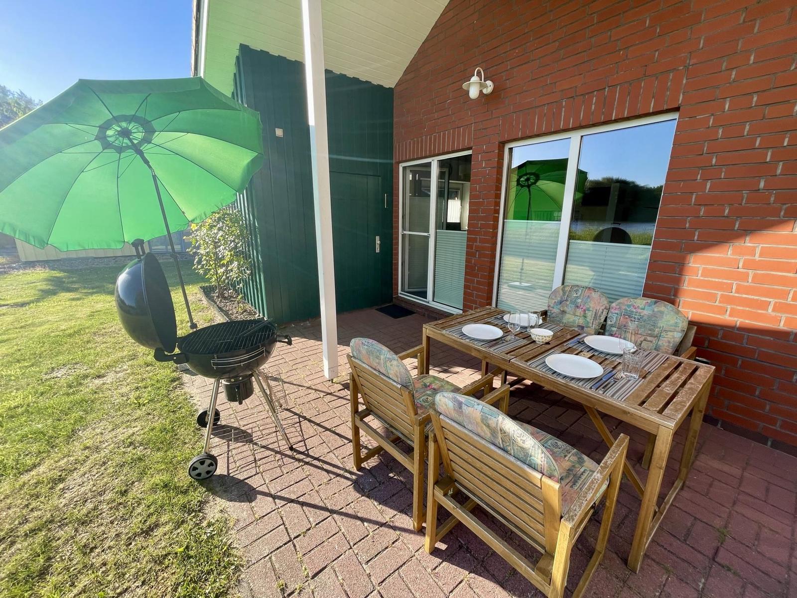 Terrace with table, chairs, grill, and green umbrella.