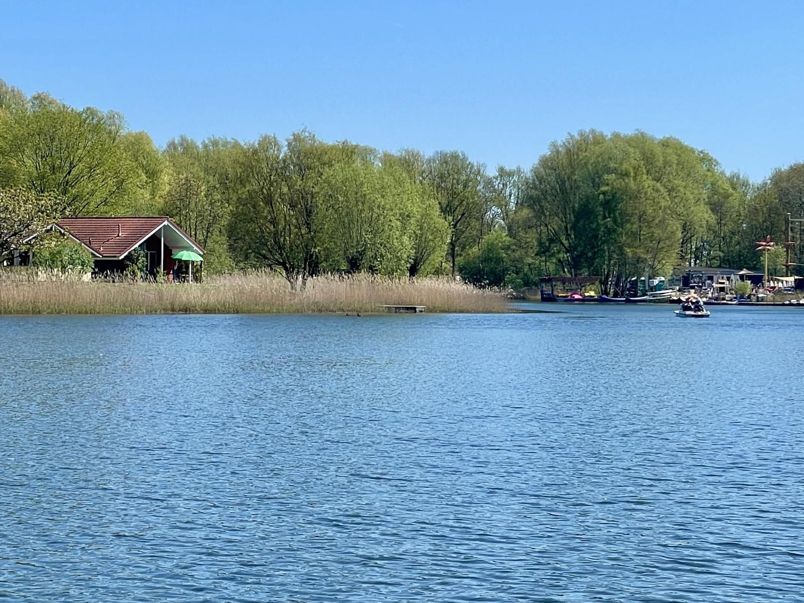 A lake with boats and a house on the shore among trees.