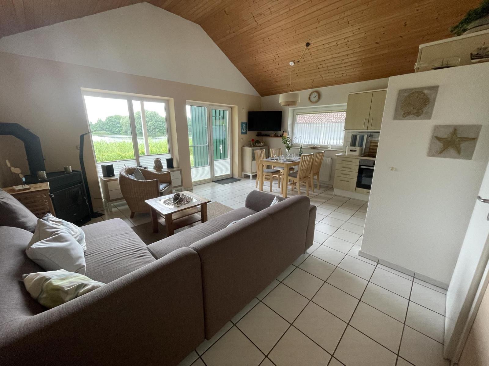 Living and dining area with kitchen, wooden ceiling, and large window. Furniture is present.