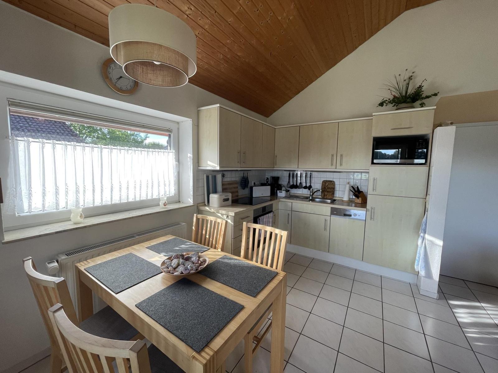 Kitchen with dining table, wooden ceiling, and window with curtains.