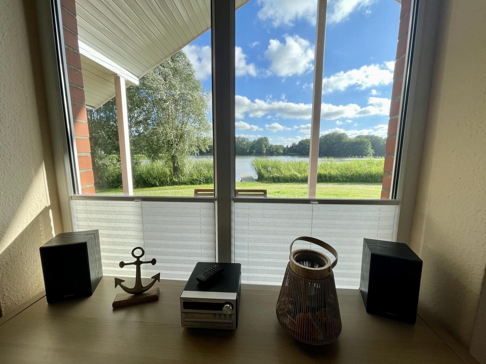 View of a lake through large windows with audio equipment on a table.