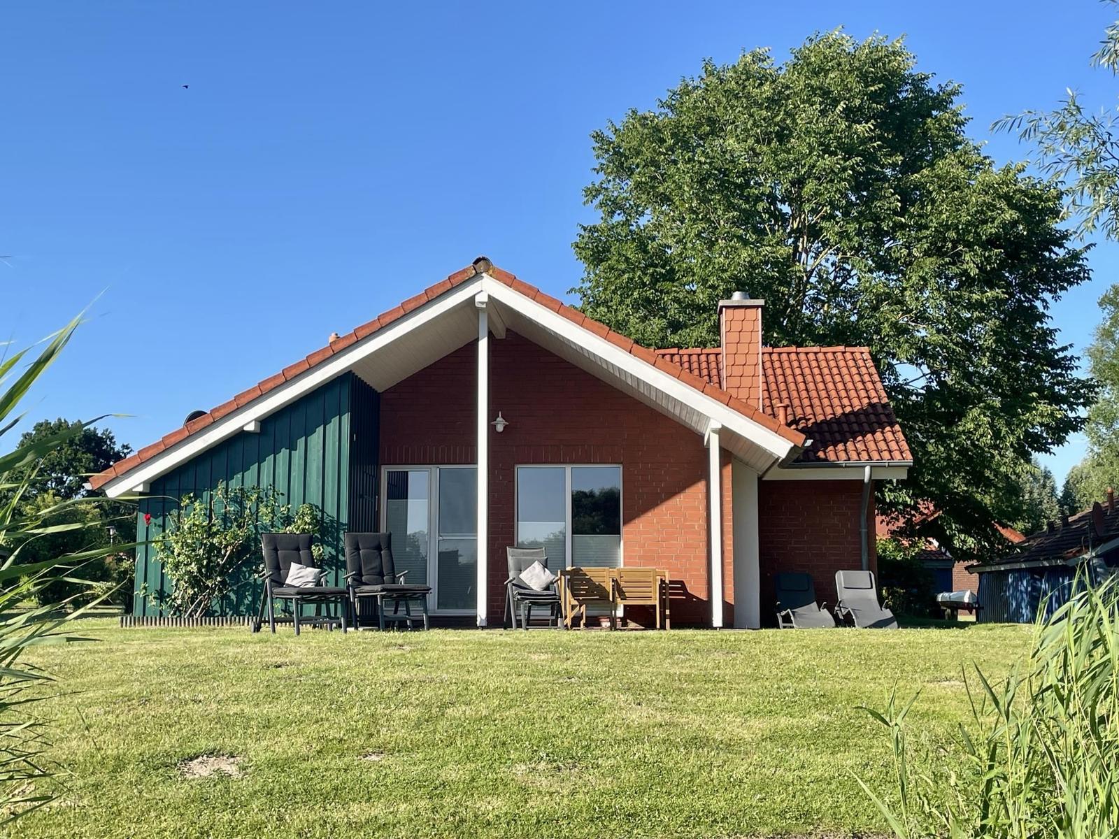 A house with a red roof and green extension. Outdoor furniture is on the lawn.