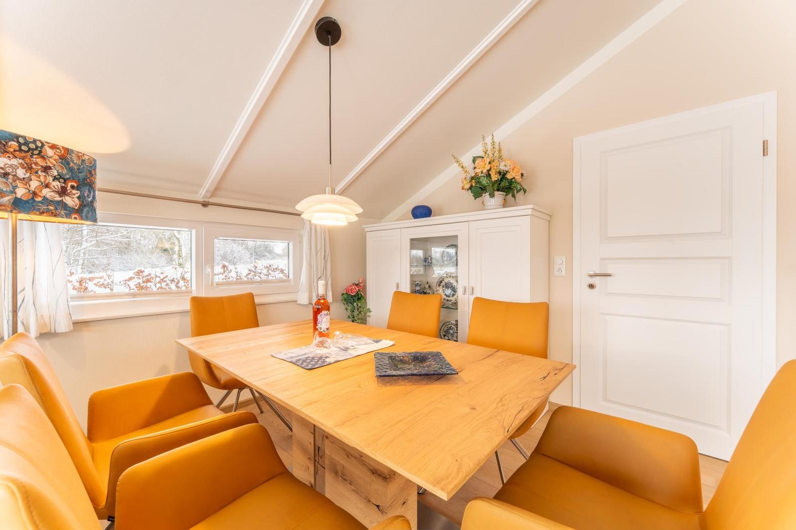Dining room with wooden table, orange chairs, and view of snow.