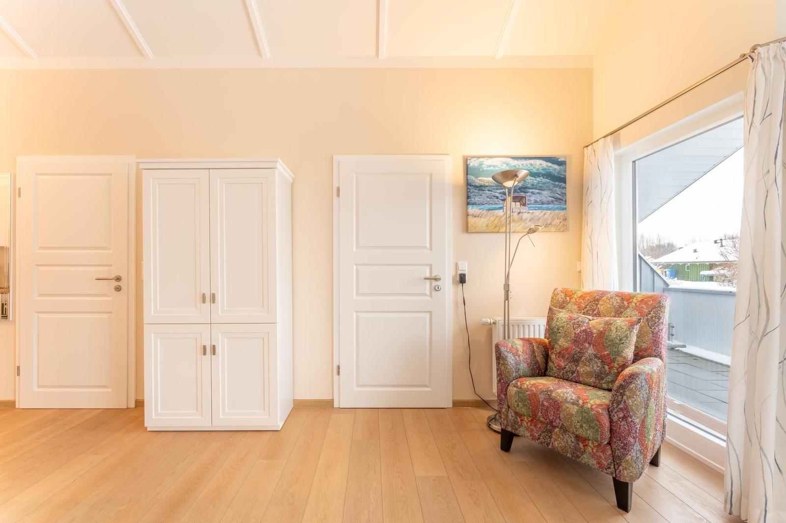 Room with white doors, wardrobe, armchair, and window to terrace.