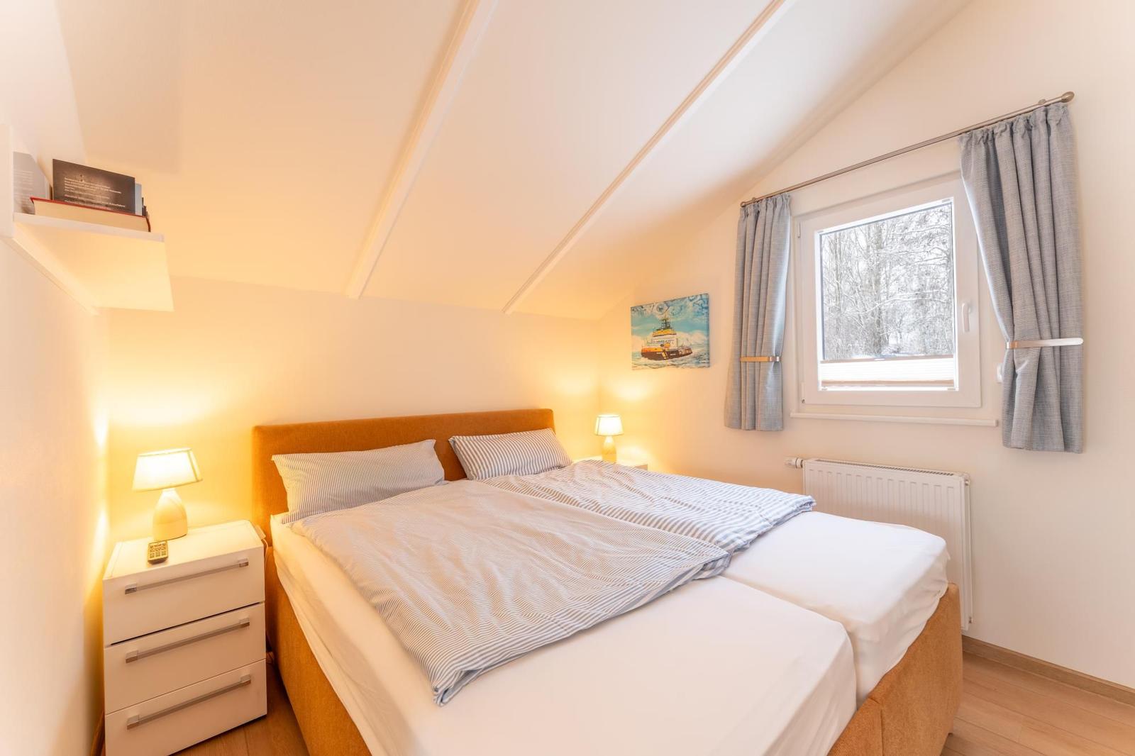 Bedroom with double bed, nightstand, window, and warm lighting.