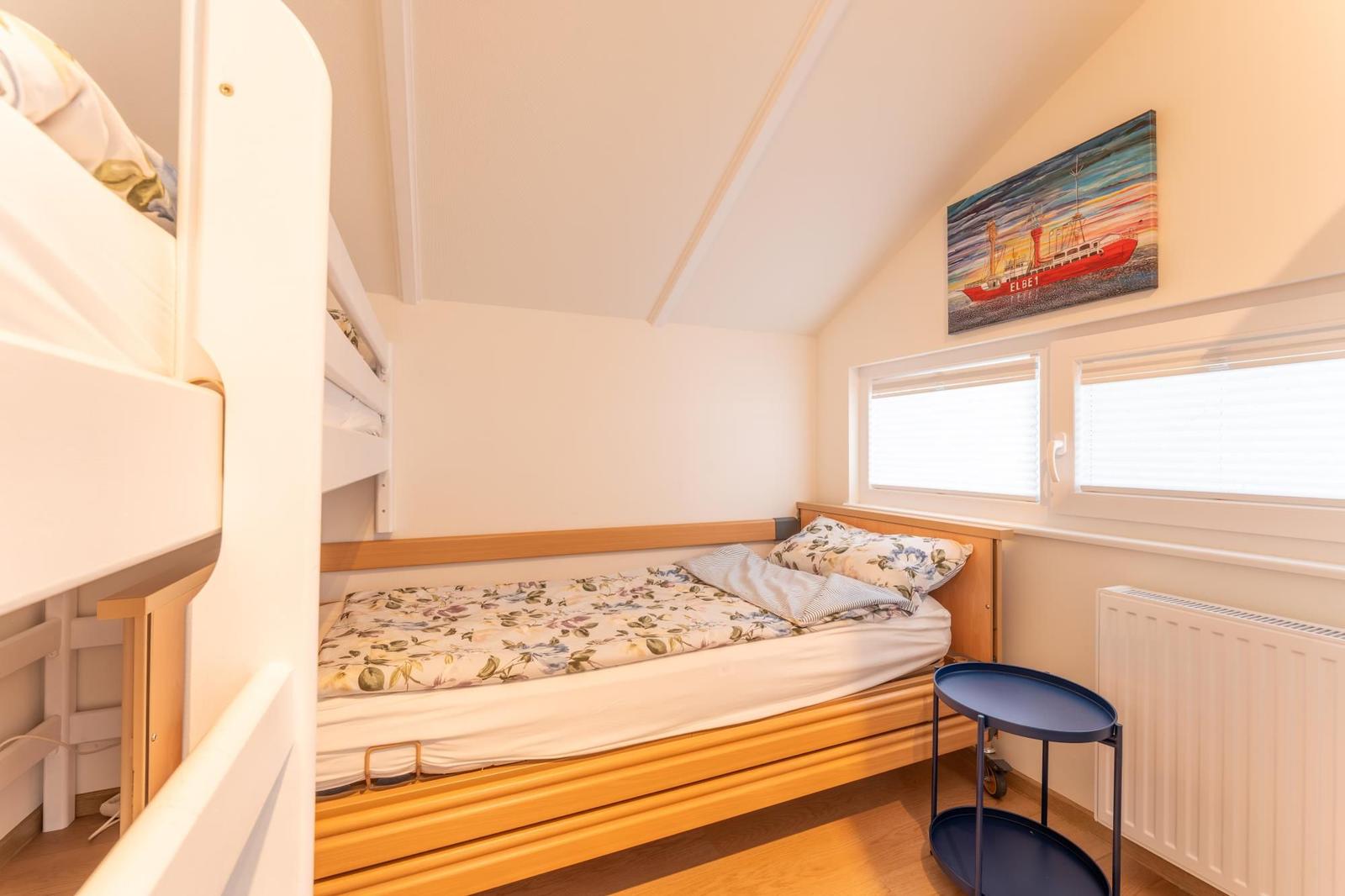 Room with double bed, radiator, and windows with blinds.