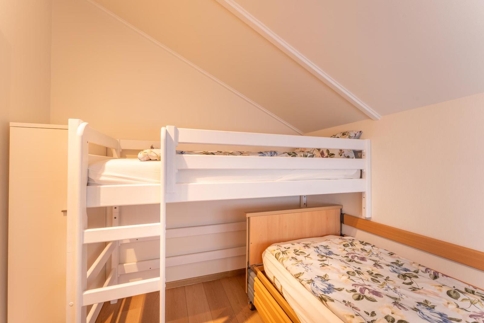 Room with bunk bed and single bed under sloped ceiling.