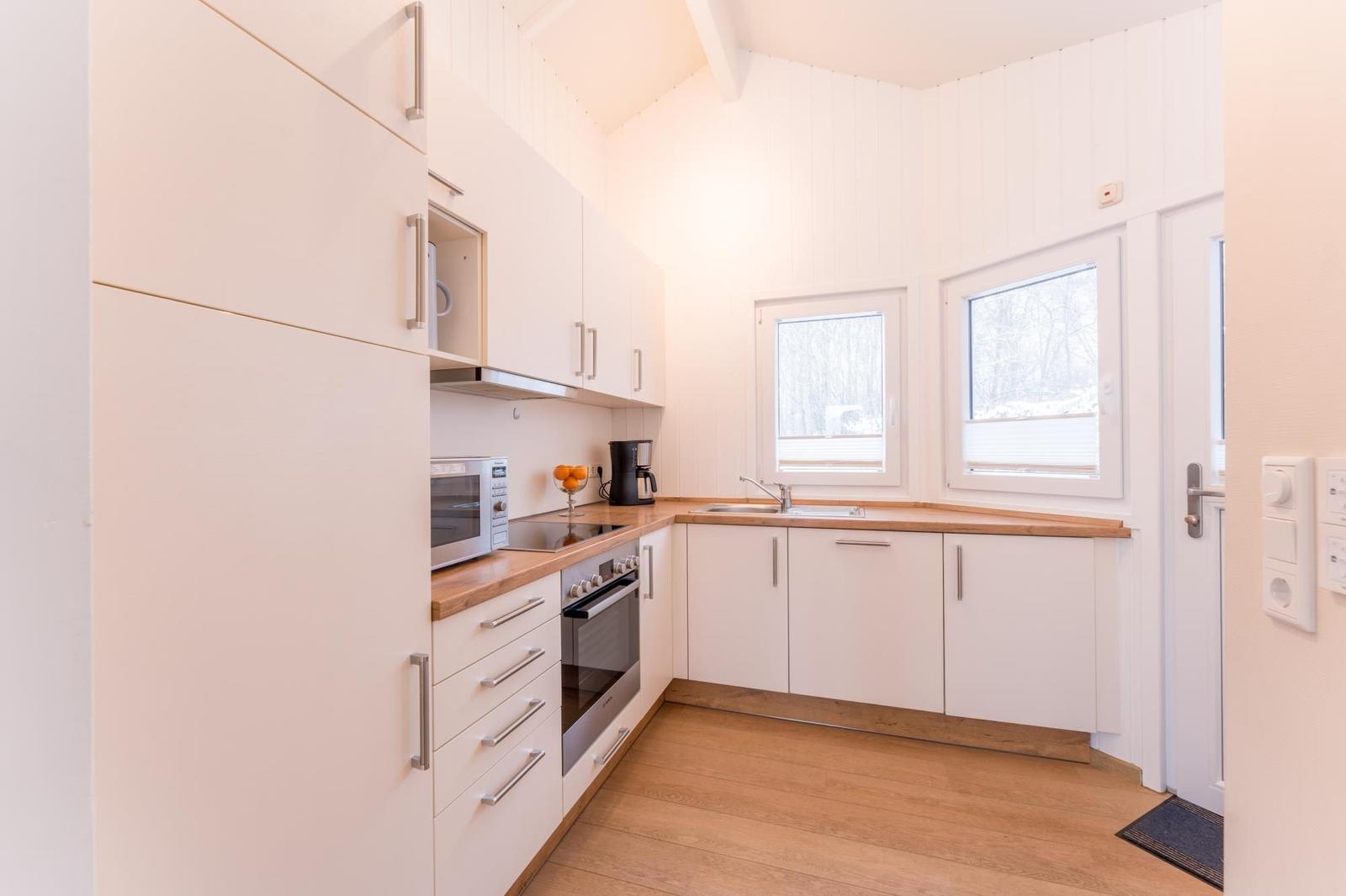 Kitchen with white cabinets, wooden countertops, and windows for outside view.